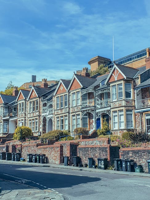 A multi-storey red brick residential building with white-framed windows and a tiled roof, situated on a street with pedestrians and parked cars. The building's exterior shows some weathering, with sha